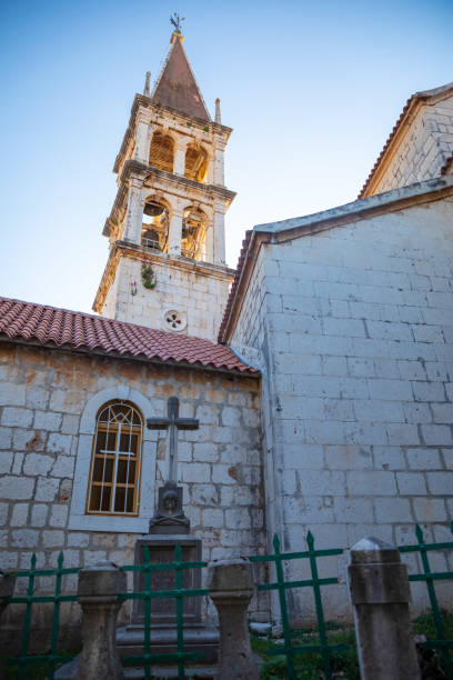 Bell tower of the Church of Our Lady of the Annunciation at the end of a narrow street in the town of Milna on Brac island, Dalmatia, Croatia Milna, Croatia - April 1, 2021: Bell tower of the Church of Our Lady of the Annunciation at the end of a narrow street in the town of Milna on Brac island in Dalmatia, Croatia old catholic church on island brac croatia stock pictures, royalty-free photos & images