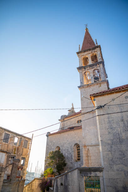 Bell tower of the Church of Our Lady of the Annunciation at the end of a narrow street in the town of Milna on Brac island, Dalmatia, Croatia Milna, Croatia - April 1, 2021: Bell tower of the Church of Our Lady of the Annunciation at the end of a narrow street in the town of Milna on Brac island in Dalmatia, Croatia old catholic church on island brac croatia stock pictures, royalty-free photos & images
