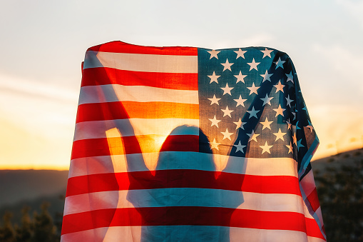 Día de la Independencia. Silueta de mujer sostiene una bandera americana en sus manos, izada sobre su cabeza. Vista trasera. Al fondo, puesta de sol y montañas. El concepto de American National Holidays photo