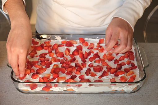 Strawberry tiramisu cake making. Womans female hands laid strawberries on the cake Italian food concept