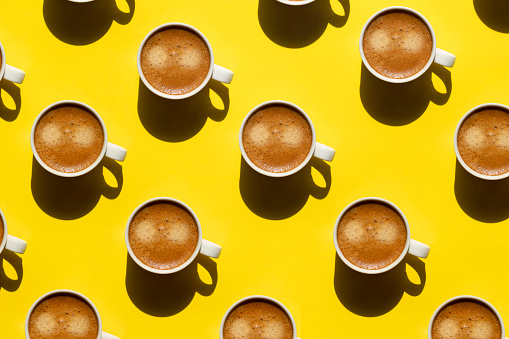Pattern made of cup of cappuccino on yellow background