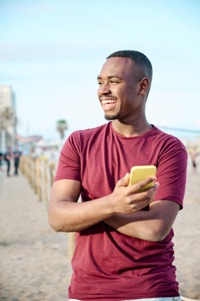istock young black man at the beach smiling and using his smartphone 1318321216