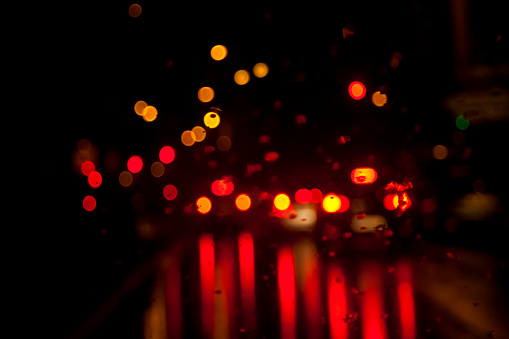 Street view at night, raining, red traffic lights, tail lights, street lights and reflections in a row, raindrops in the foreground, city life.