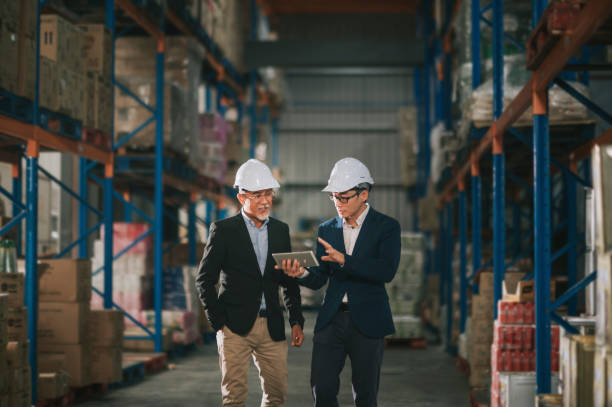 asian chinese management having discussion at warehouse with white hardhat using digital tablet