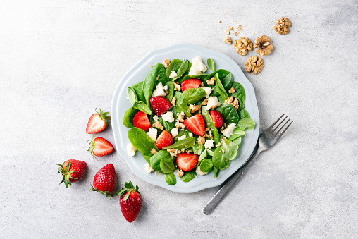 Salad with strawberries, feta cheese and walnuts. Healthy diet low calorie salad on plate, grey concrete background, top view