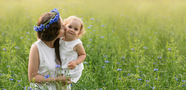 Mother and daughter in a field of cornflowers at sunset. The mother's care and love for the child. Love and parenthood. Mother's Day is a family holiday. Banner