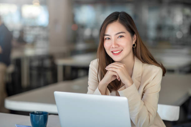 encantadora empresária asiática trabalhando com um laptop no escritório. olhando para a câmera. - asia - fotografias e filmes do acervo