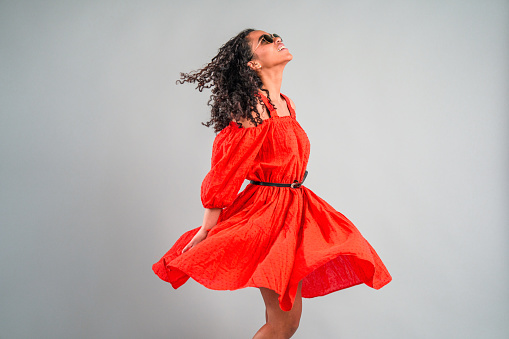 Portrait of young Hispanic woman dancing in studio on white background. She is  wearing dresses and partying.