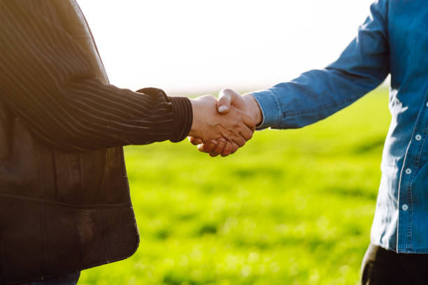 istock Handshake two farmer after agreement.  Two farmer standing and shaking hands in a  green wheat field. 1318333621