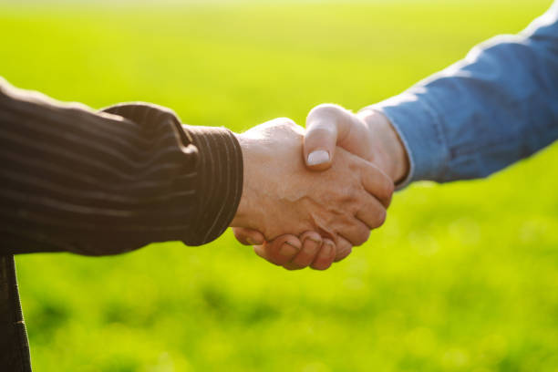 istock Handshake two farmer after agreement.  Two farmer standing and shaking hands in a  green wheat field. 1318333622