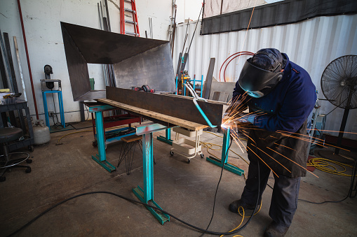 A lone welder uses his angle grinder in his shop.