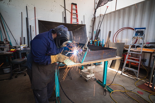 A lone metal worker uses his angle grinder in his shop.