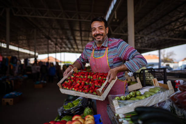 Strawberry fields forever! Portrait of male farmer holding a crate full of strawberries at the marketplace. market vendor stock pictures, royalty-free photos & images