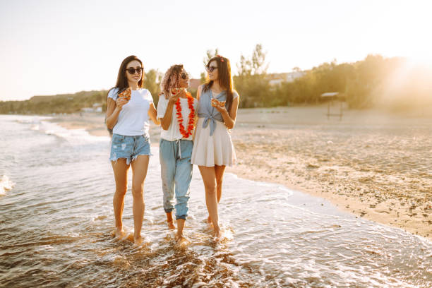 istock Three young woman spending time together at the beach, having picnic, eating pizza. 1318336832