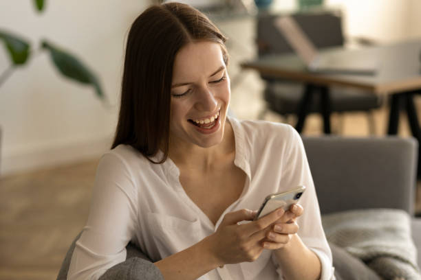 istock Smiling young caucasian millennial woman chatting in social networks using mobile applications sitting on couch at home 1318336975