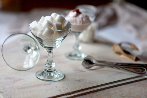 White Refined Sugar Cubes in the sugar-bowl angle view on wooden background. vintage glass, sugar cubes on a wooden table. Ice Cream cup for Dessert Cake Juice. Shabby chic style decorations. European Vintage Embossed Bowl Creative Glass