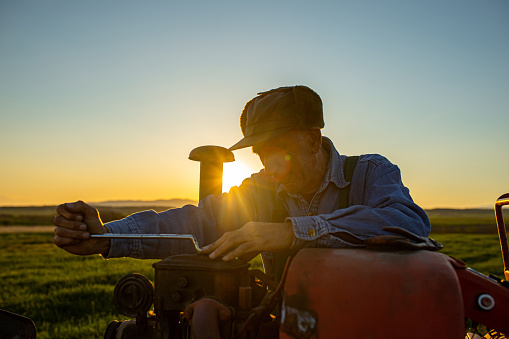 Photo of mature farmer fixing tractor outside in the field
