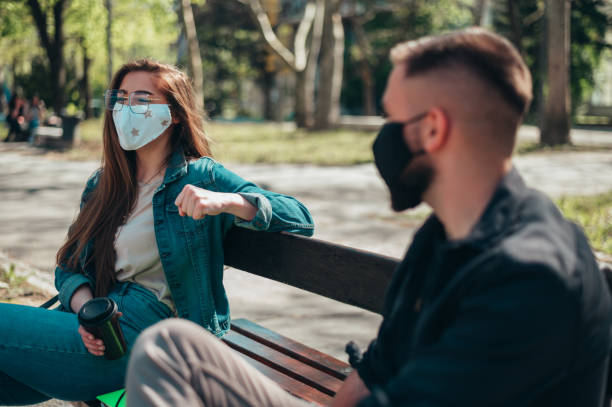 istock Two young students wearing protective mask and sitting on a bench while making a distance 1318349473