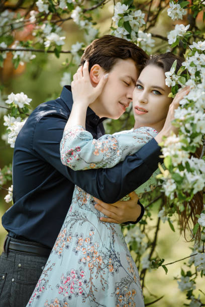 jovem casal bonito abraçando-se em uma árvore flores de cerejeira florescendo. - portrait adults apple tree cherry tree - fotografias e filmes do acervo