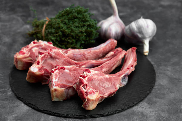 istock Raw lamb chops with garlic, herbs on black ceramic plate over white stone gray table. Top view. With copy space 1318351569