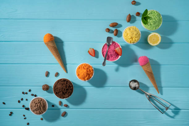 istock Assorted ice cream cups in a row and waffle cones colorful on blue wood background 1318351633