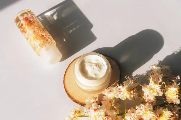 Cream jar and Horse chestnut flowers on white table in sunlight. Natural organic cosmetics concept. Long harsh shadows, top view.