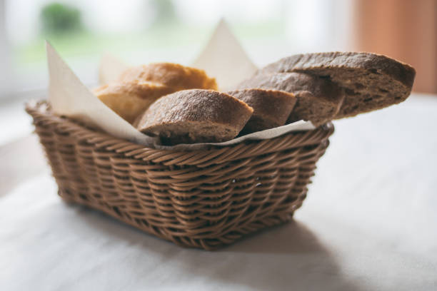 istock Partially blurred wicker basket with black and white bread on white tablecloth near the window 1318364618