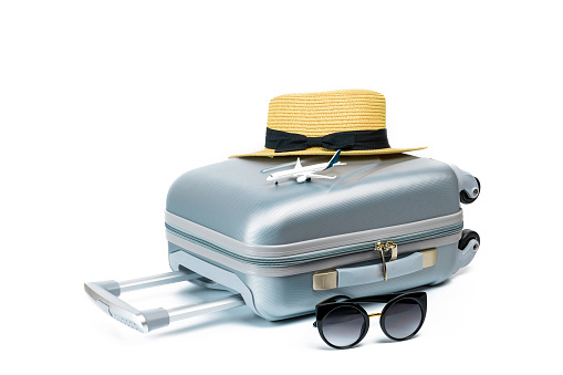 Tropical background. Suitcase, sunglasses with toy plane and straw hat in travel composition isolated on white background. Exotic tropical beach with copy space