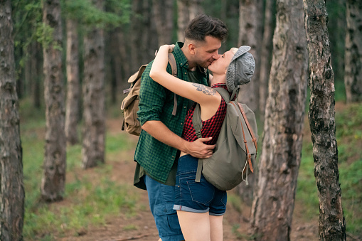 Man and woman, happy young couple, kissing and hugging on the forest trail.