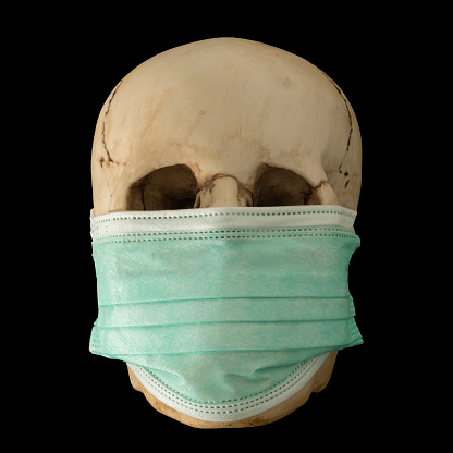A protective surgical face mask being worn by a human skull, on a black background, as a concept of protection against the Covid 19 virus pandemic and the importance of wearing a face mask.