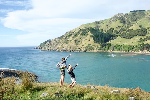 Two boys in a rural coastal landscape with their hands raised in the air. Taken at Cable Bay, a local landmark for the Nelson Region of New Zealand's South Island.