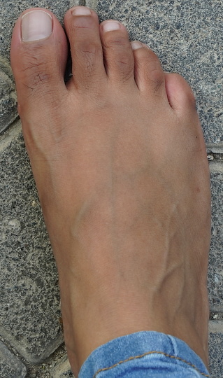 Foot is ugly, dark brown and it has hair and veins showing. No manicure. unmanicured nails.