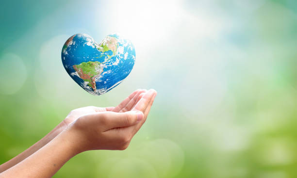 World environment day concept: man opens palms and drags heart shaped earth globe over blurred blue sky and water background. Elements of this image furnished by NASA stock photo