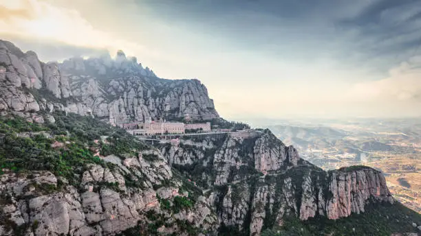 Abbey of Montserrat Panorama. Sunset twilight over the Santa Maria de Montserrat Monastery. Famous Benedictine Monastery under harsh cliffs in the mountains near Barcelona. Initial construction of the basilica of Montserrat began in the 16th century, at 1236m (4055 ft) above the valley floor, Montserrat is the highest point of the Catalan Lowlands. Montserrat, Barcelona, ,Catalonia, Spain, Southern Europe