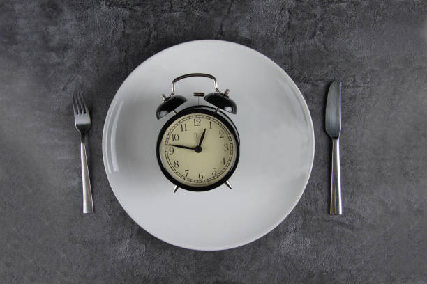 istock alarm clock on a plate, fork and table knife isolated on gray background. Image contains copy space 1318393068