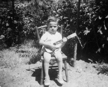 Image taken in the early sixties, Little boy playing guitar at his backyard