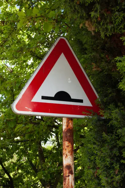 A rusty retarder sign is partially hidden in the vegetation of a green hedge.