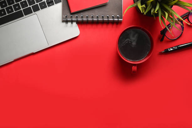istock Above view laptop computer, houseplant, coffee cup, glasses and notebook on red background. 1318394083