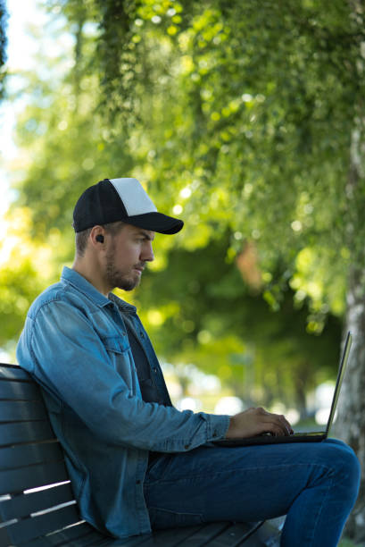 istock Young man using wireless earbuds and laptop. He is sitting on a park bench 1318394965