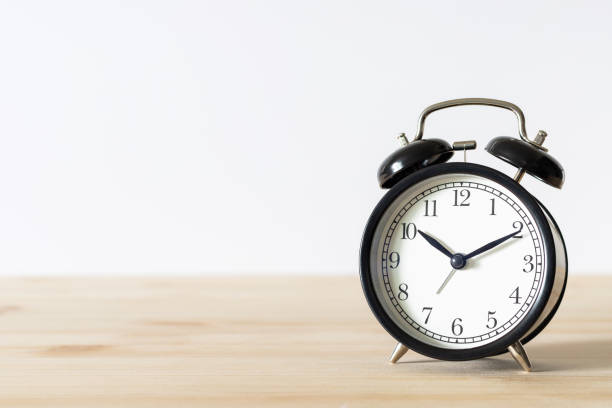 istock Classic black alarm clock on wooden table with white background and copy space 1318397872