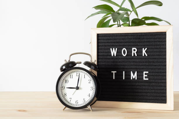 istock Classic black alarm clock on wooden table and black board with words 'work time' with white wall background and copy space. 1318397874