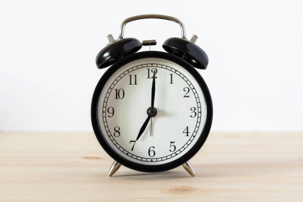 istock Classic black alarm clock on wooden table with white background and copy space 1318397883