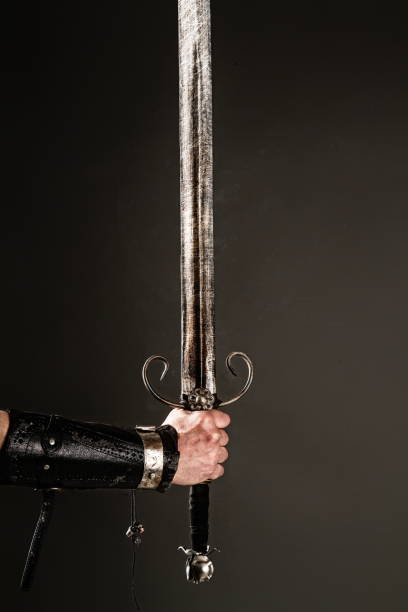 hand holding sword hand in armor holding a huge knightly sword on a dark background chivalry stock pictures, royalty-free photos & images