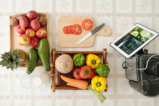 Tray with fresh vegetables, cutting board, knife and tablet computer with recipe on screen, viw from the top