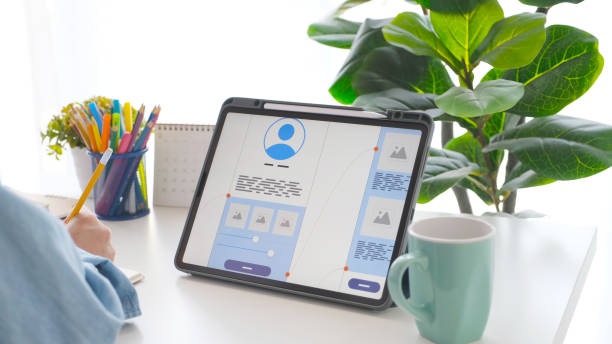 istock Man hand holding pencil and digital tablet with mobile app development prototype on screen while working at home 1318405793