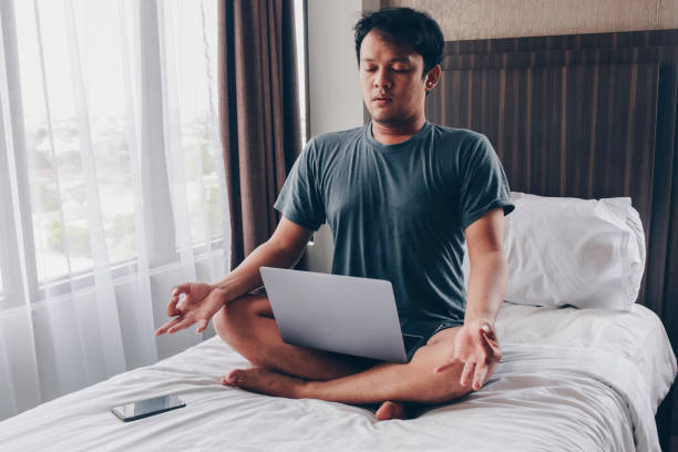 istock Work from home. Young Asian man sits on a bed. Home workplace. Break, relaxation at the time of work. 1318406036
