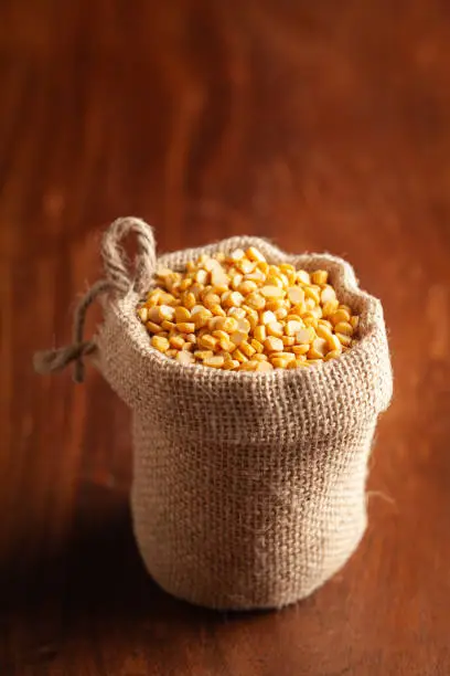Close-up of Organic Bengal Gram (Cicer arietinum) or split yellow chana dal in a standing jute bag over wooden brown background.