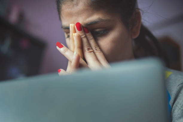 Stressed tired young woman using a laptop to work from home. Indoor low angle image of a tensed worried young woman feeling tired during working on the laptop at home. cyberbullying stock pictures, royalty-free photos & images