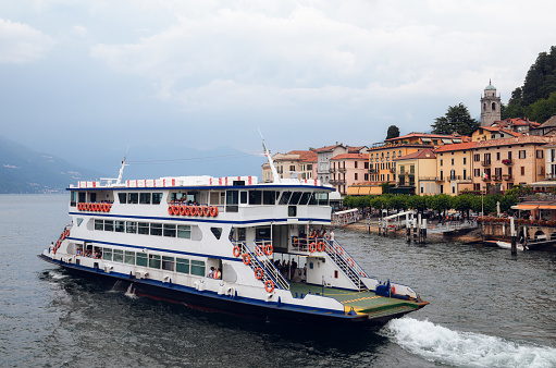 Cloudy misty morning view of the harbor and village of Bellagio, small town on the Como Lake, Italy, with calm water and a ferry boat sailing