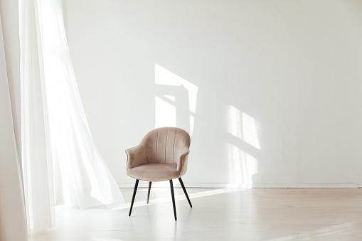 beige chair in the interior of an empty white room with a window